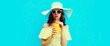 Portrait of beautiful young woman drinking a fresh juice wearing a summer hat on blue background