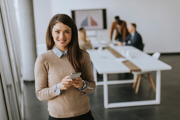 Young business woman standing in the office and using mobile phone in front of her team