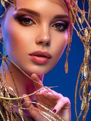 Wall Mural - Stylish fashion model with a golden decoration around her face. Beauty style. Art portrait of a beautiful woman with bright makeup. Closeup model face with vivid eye make-up.