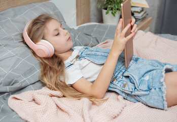 Poster - Cute Little girl lying on bed and using tablet at home