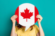 © Evgenia - girl holds blank white speech bubble with canadian flag isolated on blue background. Invitation to study in Canada concept