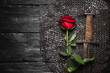 Knight sword and red rose flower on the black wooden flat lay background with copy space.