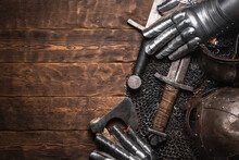 Medieval Concept Flat Lay Background With Copy Space. Sword, Helm, Chain Mail And Gloves On The Wooden Table Top View.
