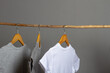 Cotton clothes in natural colors hang on a wooden hanger on a gray background