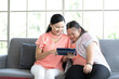 mother using tablet computer with a girl down syndrome or her daughter, smiling and enjoying on sofa