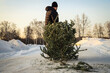A man drags an used Christmas tree to the dumpster. After Christmas. Snowy winter. Outdoors. Selective focus