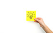 A yellow sheet for notes with a painted light bulb is held in your hand