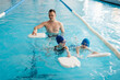 © Andrii - A group of boys and girls train and learn to swim in a modern swimming pool with an instructor. Development of children's sports. Healthy parenting and promotion of children's sports.
