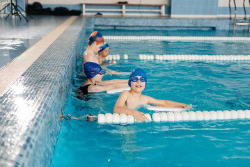 A group of boys and girls train and learn to swim in a modern swimming pool with an instructor. Development of children's sports. Healthy parenting and promotion of children's sports.