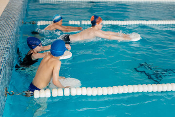 A group of boys and girls train and learn to swim in a modern swimming pool with an instructor. Development of children's sports. Healthy parenting and promotion of children's sports.