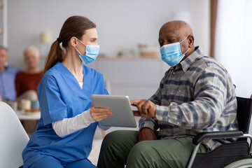 Wall Mural - Female nurse helping black senior man using digital tablet