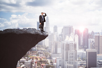 Canvas Print - Handsome young european businessman on cliff edge looking into the distance on bright city background with daylight and mock up place. Future, success, leadership and career growth concept.