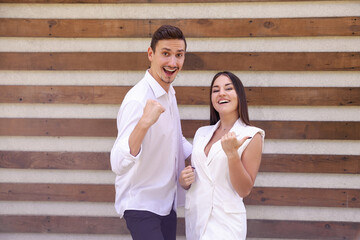 emotions, lifestyle, gesture and people concept - Happy joyful Caucasian couple in white clothes winning a prize on a brown ribbed background with copy space