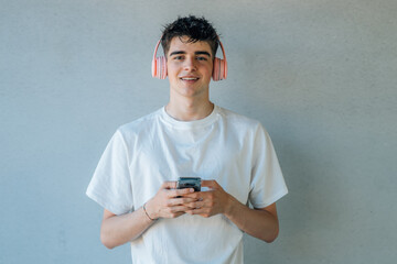 Poster - teen boy with mobile phone and headphones listening to music isolated on wall with copy-space