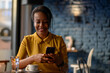 © Zamrznuti tonovi - African american woman using airpods and a smartphone while sitting in a cafe