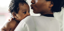 Portrait Of Enjoy Happy Love Family African American Mother Playing With Adorable Little African American Baby.Mom Kiss With Cute Son Moments Good Time In A White Bedroom.Love Of Black Family