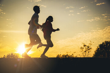 Wall Mural - Silhouette of young couple running together on road. Couple, fit runners fitness runners during outdoor workout with sunset background.	