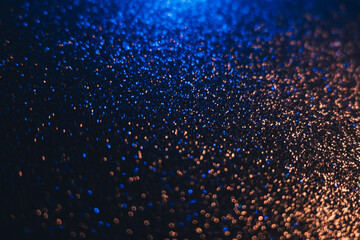 Color bokeh glow. Glitter background. Wet asphalt reflection. Defocused neon blue bronze light shiny sparkles round flecks texture on dark black abstract overlay.