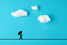 Stickman Walking With Umbrella Under The Fluffy Rain Clouds Made Out Of Cotton On Blue Sky Background.