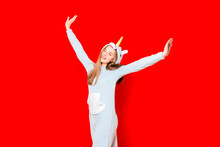 Girl In Pajamas With A Unicorn On A Red Background Raises Her Hands Up. Overnight Stay. Time To Sleep. Pajama Party. Unicorn Costume. I'm Fooling Around