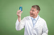© epiximages - Scientist with white coat holding small flask with blue liquid and is standing in front of green background