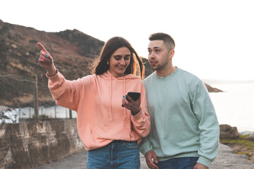 Young caucasian woman and man being guided by a smartphone at the coast.