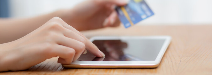 Wall Mural - Closeup hand of young asian woman holding credit card shopping online with tablet computer blank display screen buying and payment, girl using debit card purchase or transaction, e-commerce concept.