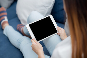 Closeup young asian woman sitting and using mockup of tablet computer with display blank screen on sofa at home, girl holding digital tablet watch entertainment at living room, communication concept.