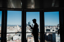 Silhouette Of Businessman Text Messaging Through Smart Phone By Glass Wall In Office