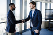 © Westend61 - Businessmen shaking hands by glass window in office