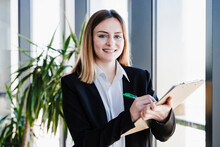 Smiling Businesswoman With Clipboard Standing In Office