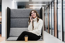 Businesswoman Talking On Smart Phone Sitting At Seat In Office