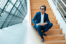 Businessman With Headphones Sitting On Steps At Office