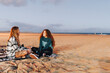 © Westend61 - Woman talking with friend sitting on sand at beach