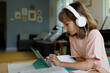 © Westend61 - Blond girl wearing headphones studying through tablet PC at home