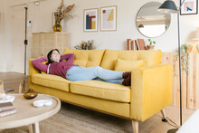 Happy Woman With Hands Behind Head Relaxing On Sofa In Living Room