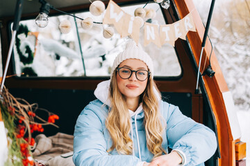 Wall Mural - Portrait of young caucasian happy woman sitting in a car in winter day, during traveling on a van and enjoying holiday.