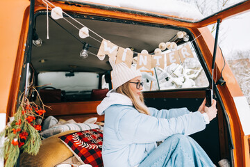 Wall Mural - Young caucasian woman taking photo, sitting in a car while traveling in road trip.