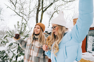 Wall Mural - Portrait of two cheerful women friends heaving fun standing outdoor near van, enjoying winter time.