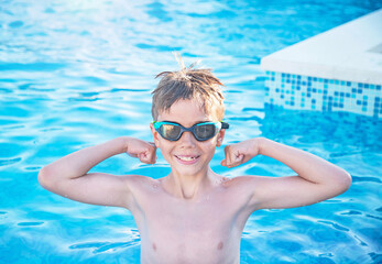 Healthy lifestyle. Active nine years old child (boy) in sport goggles in swimming pool. Child shows muscles, health force in the bent hands. Caucasian kid learn to swim.