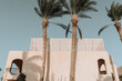 The facade of the building in a minimal arabic style. Tall palm trees. Arch-shaped windows in the wall of the building.