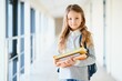 © Serhii - Front view of little beautiful school girl among corridor at school, holding notes at hands. Funny and happy girl smiling at camera, resting after lessons on primary school