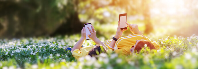 Wall Mural - Mother and her son lying down with phones on the meadow in the park