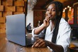 © Serhii - Young African American girl sitting in restaurant and typing on her laptop. Pretty girl working on computer at cafe.