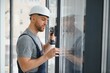 © Serhii - Workman in overalls installing or adjusting plastic windows in the living room at home