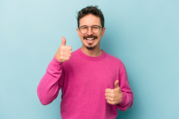 Young caucasian man isolated on blue background raising both thumbs up, smiling and confident.