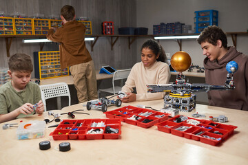 Wall Mural - Diverse group of teenage children building robots in engineering class at modern school, copy space