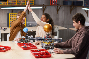 Canvas Print - Group of teenage kids high fiving while enjoying building robots in engineering class at school, copy space