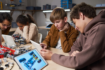 Canvas Print - Diverse group of children using digital tablets while programming robots in engineering class at modern school