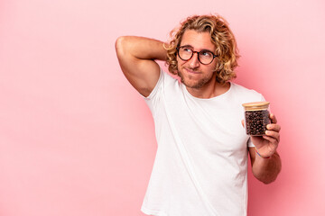 Wall Mural - Young caucasian man holding coffee jar isolated on pink background touching back of head, thinking and making a choice.